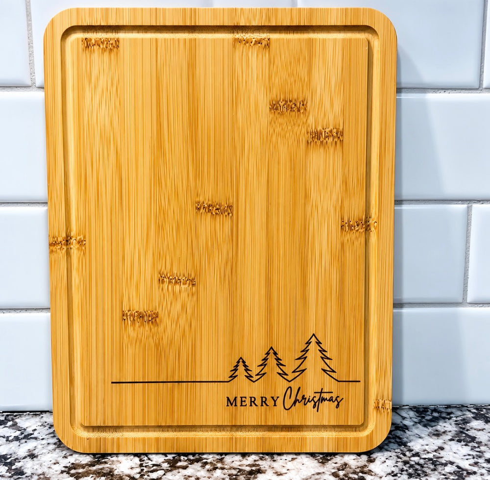 A beautiful, functional keepsake for your kitchen, hand-finished by Tiffany's Keepsake Co. This bamboo board is laser engraved with a trio of pine trees and "Merry Christmas" — perfect for holiday serving, cookie prep, or display all season long. A sweet Christmas gift for hosts, family, or friends.